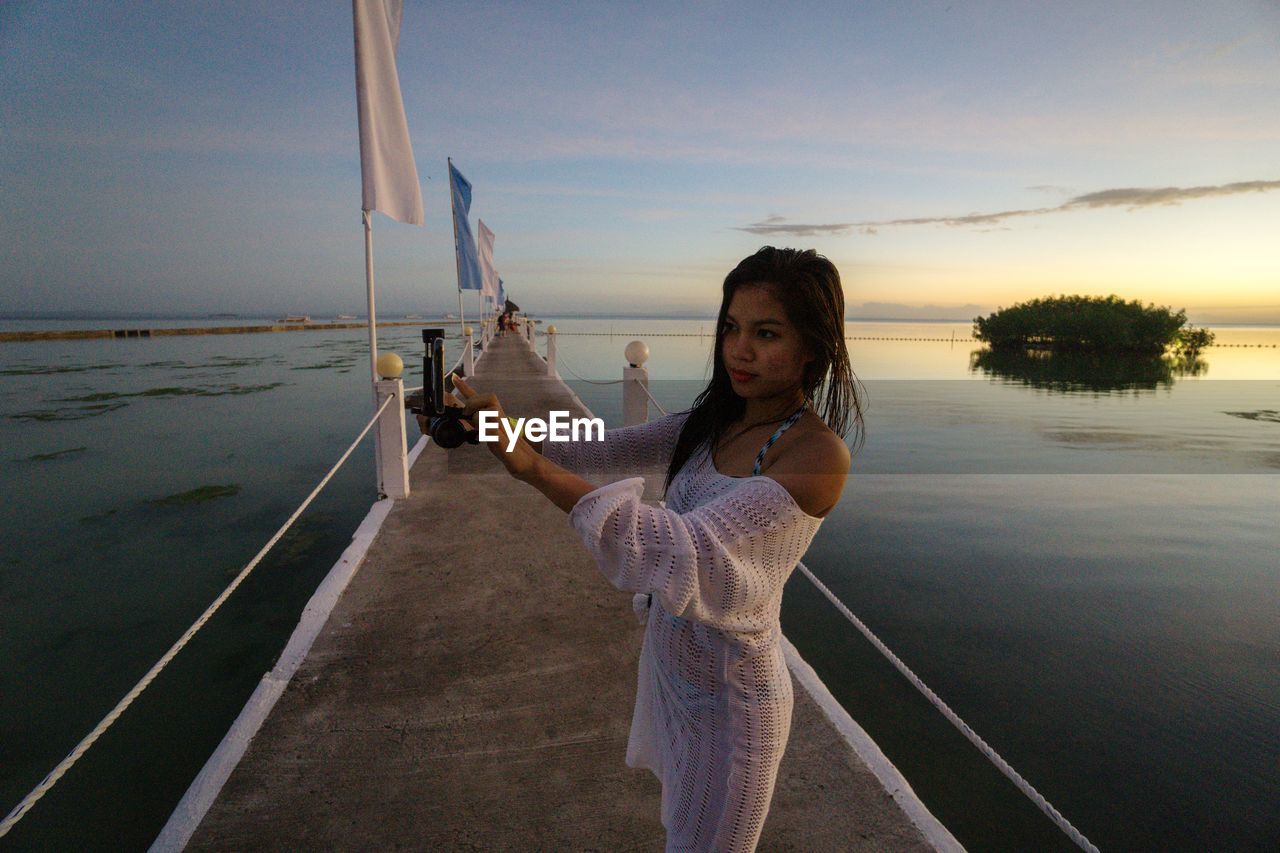 Woman standing by sea against sky during sunset