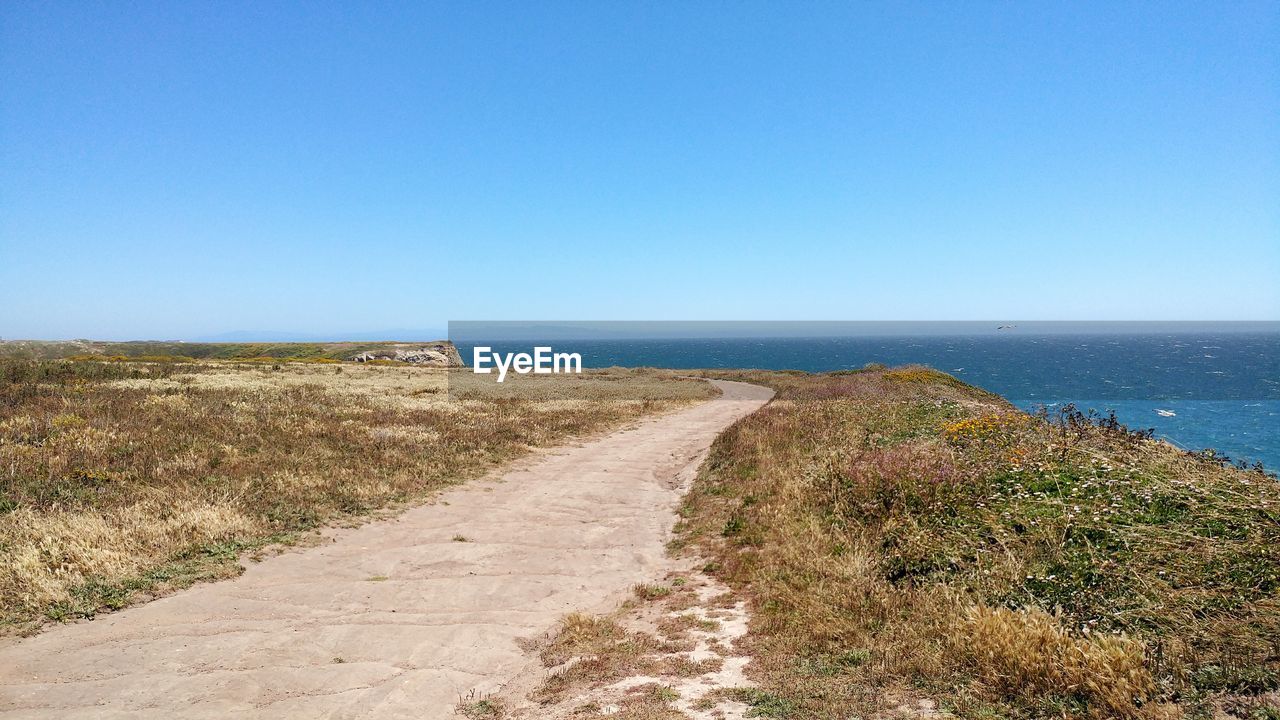 Road by sea against clear blue sky