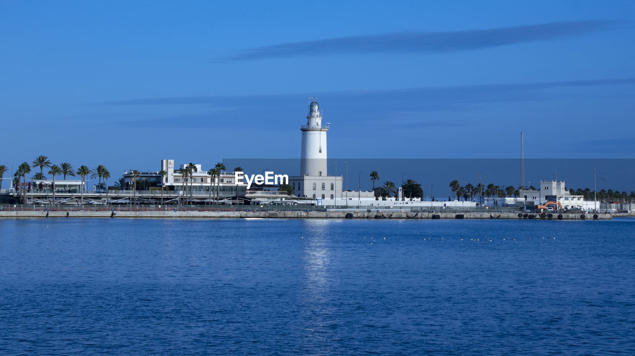 Lighthouse on sea against buildings in city