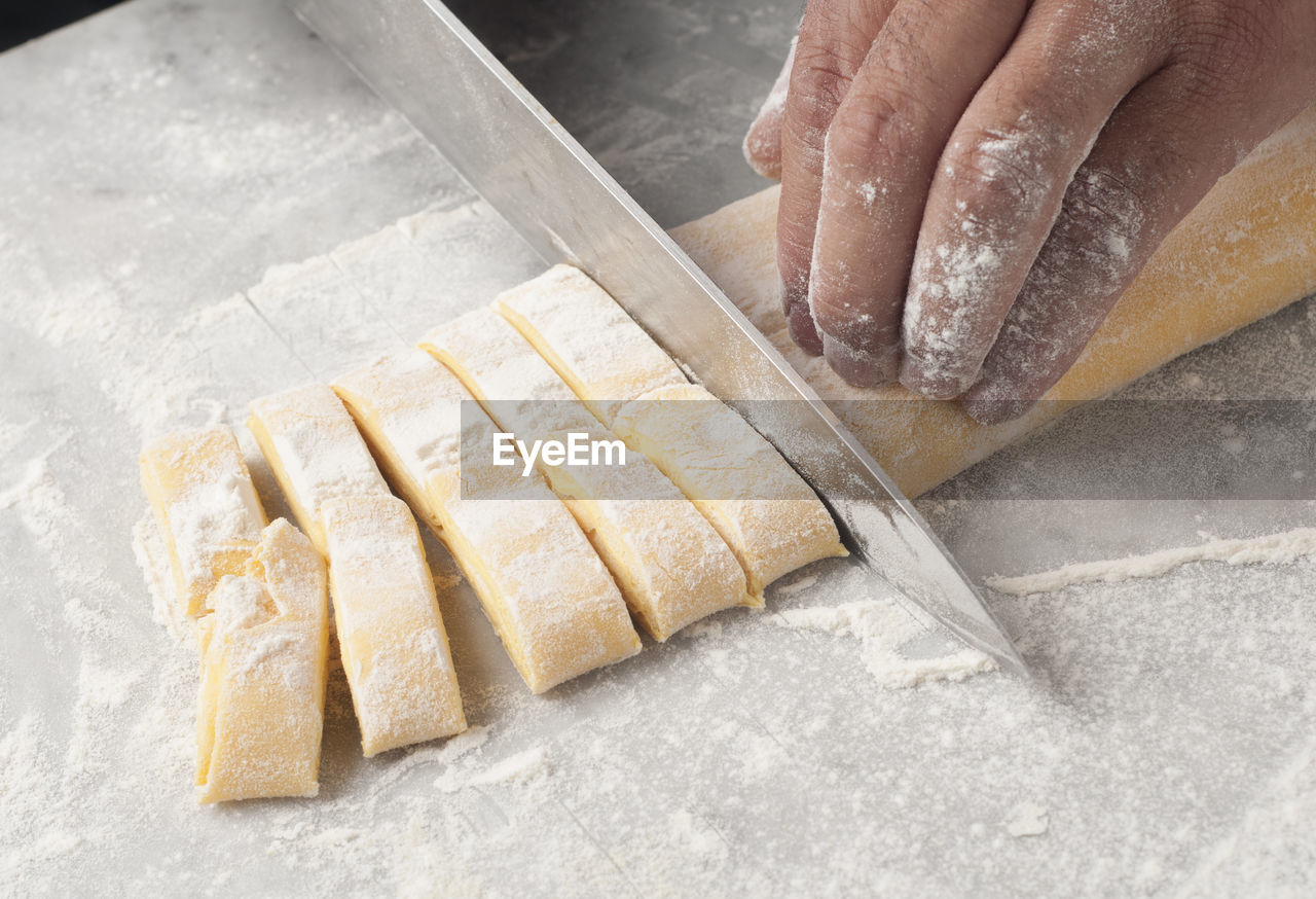 Cropped hands of chef cutting dough on table in commercial kitchen