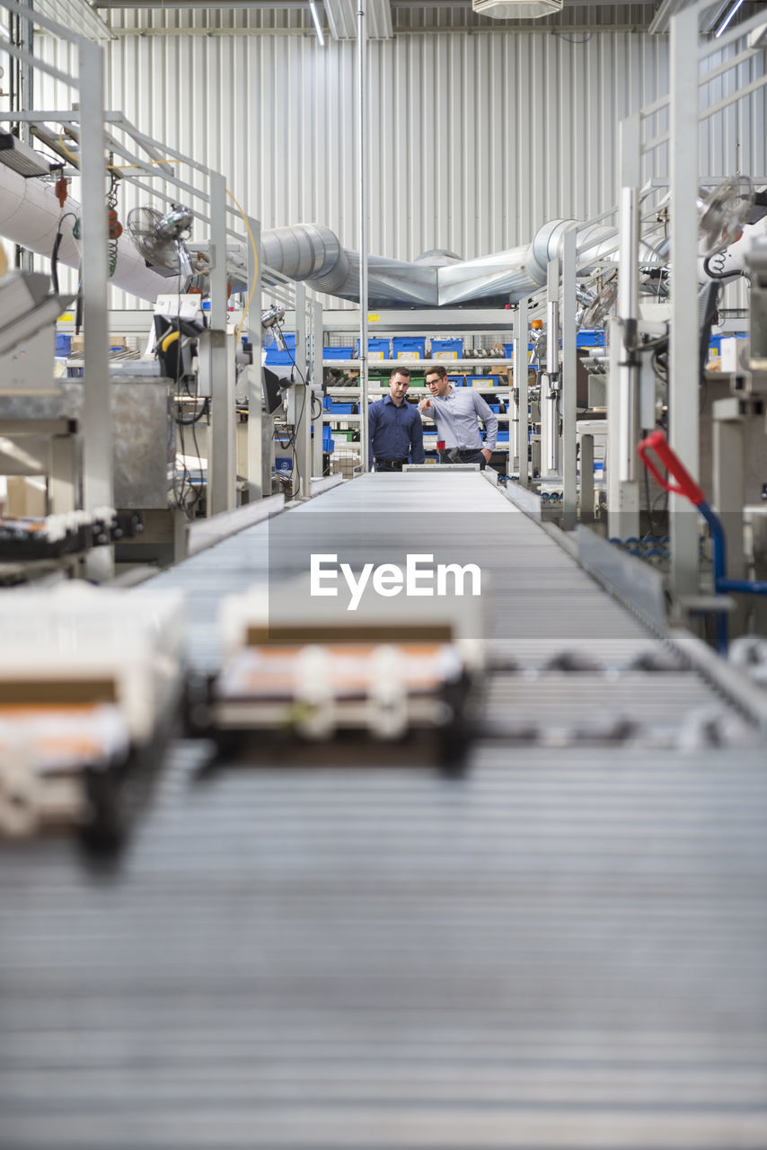 Two men talking at conveyor belt in factory shop floor