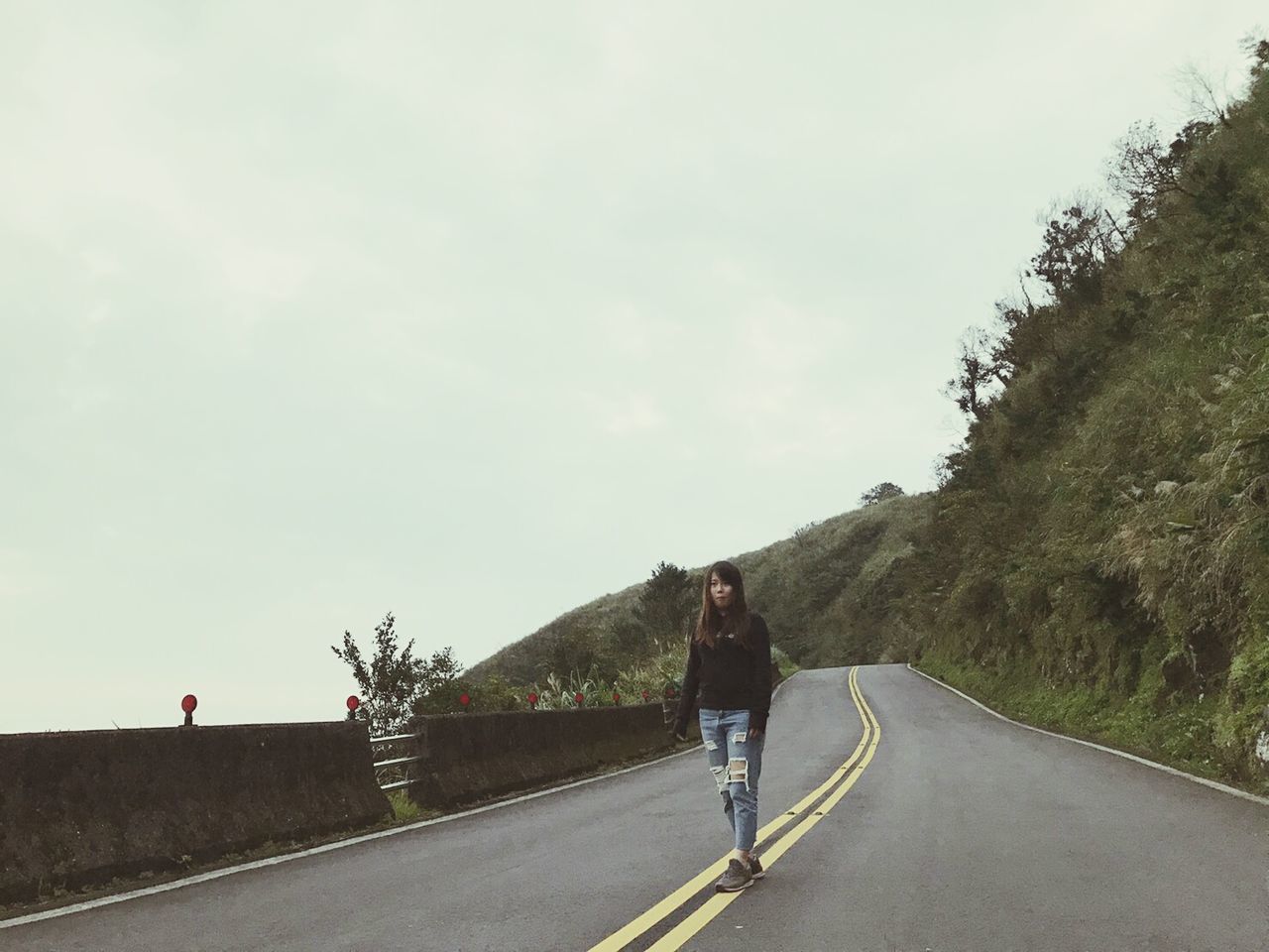 Front view of young woman walking on road by mountain against sky