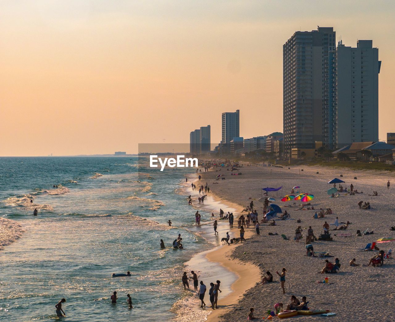 PEOPLE ON BEACH AGAINST BUILDINGS DURING SUNSET