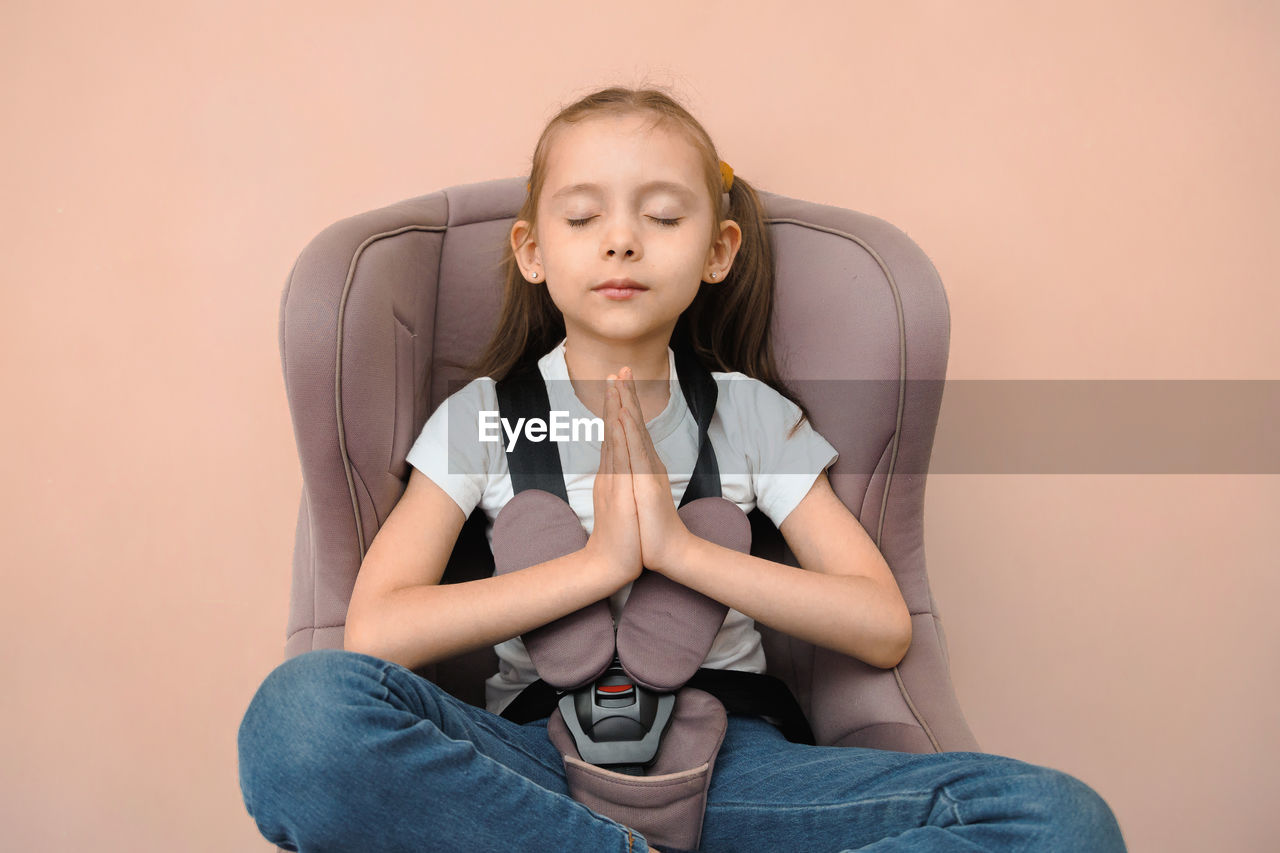 sitting, one person, child, indoors, childhood, women, person, relaxation, front view, portrait, lifestyles, portrait photography, adult, female, studio shot, photo shoot, casual clothing, emotion, clothing, human face, human leg, copy space, cross-legged, three quarter length, looking at camera, looking, sadness, colored background, contemplation, limb