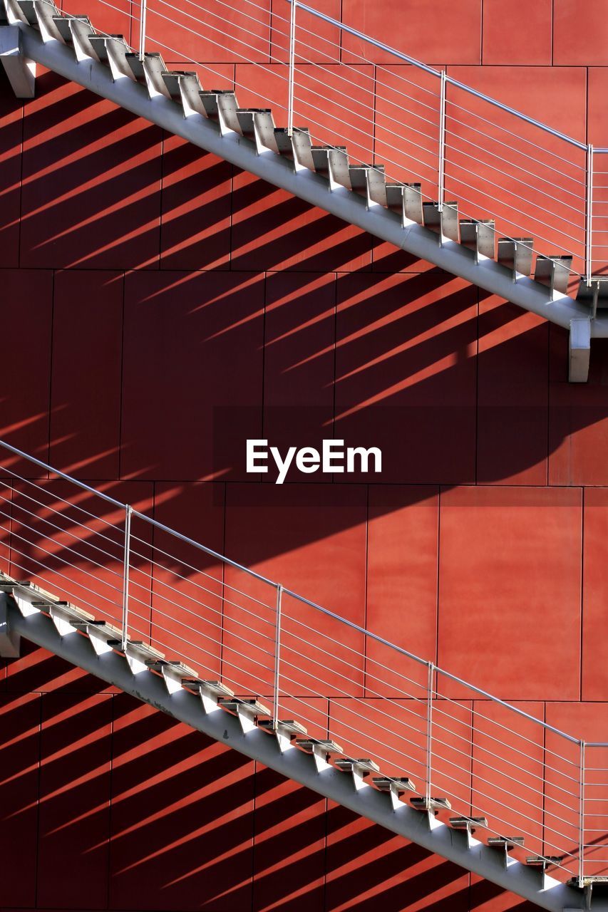 Low angle view of steps and staircases on red wall during sunny day