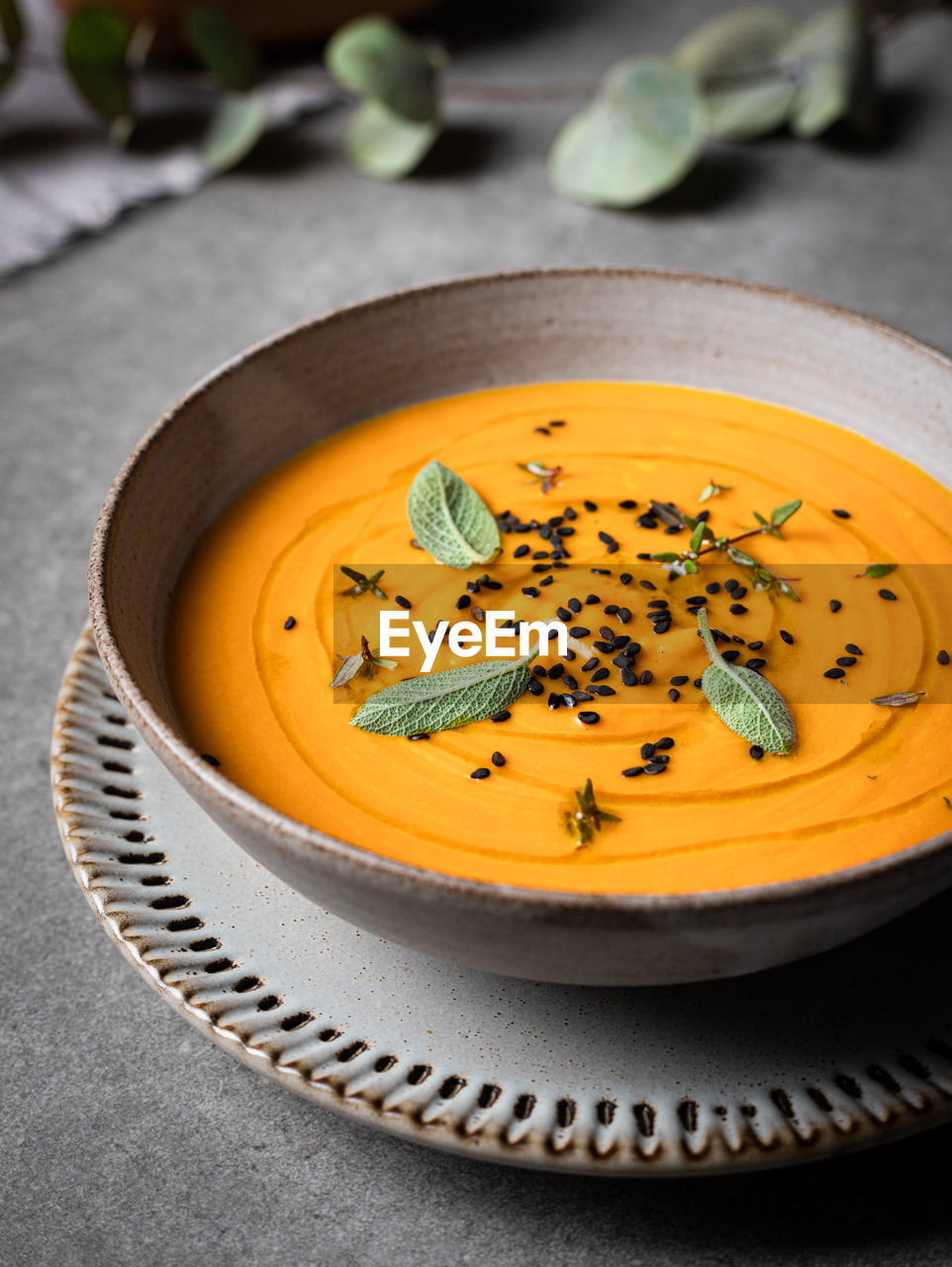 From above of bowl with delicious pumpkin soup served with seasonings on gray table in restaurant