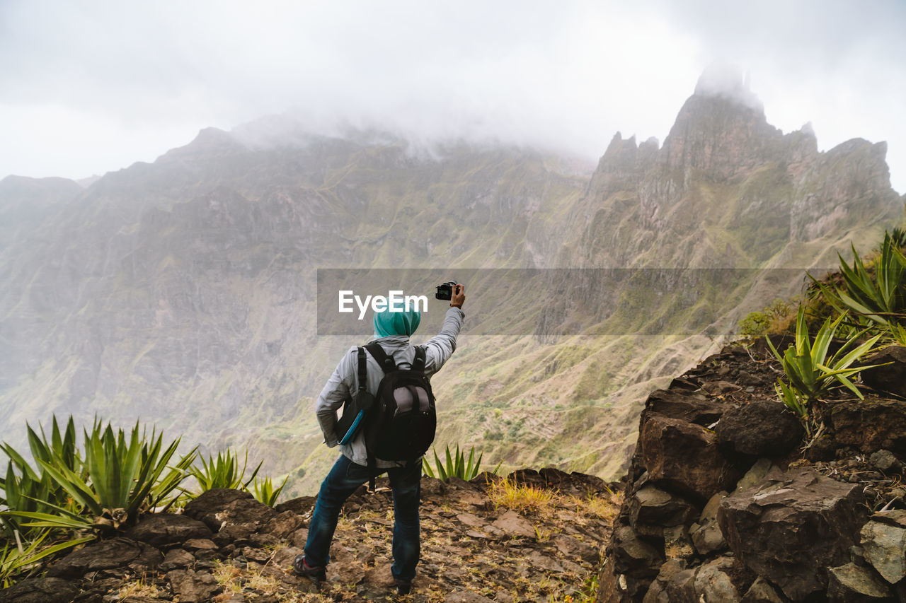 Rear view of man photographing while standing on mountain