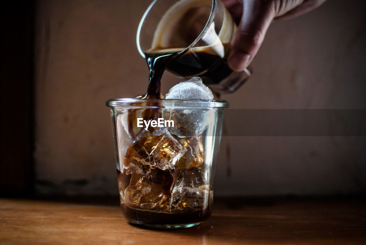 Cropped image of person pouring coffee on drinking glass
