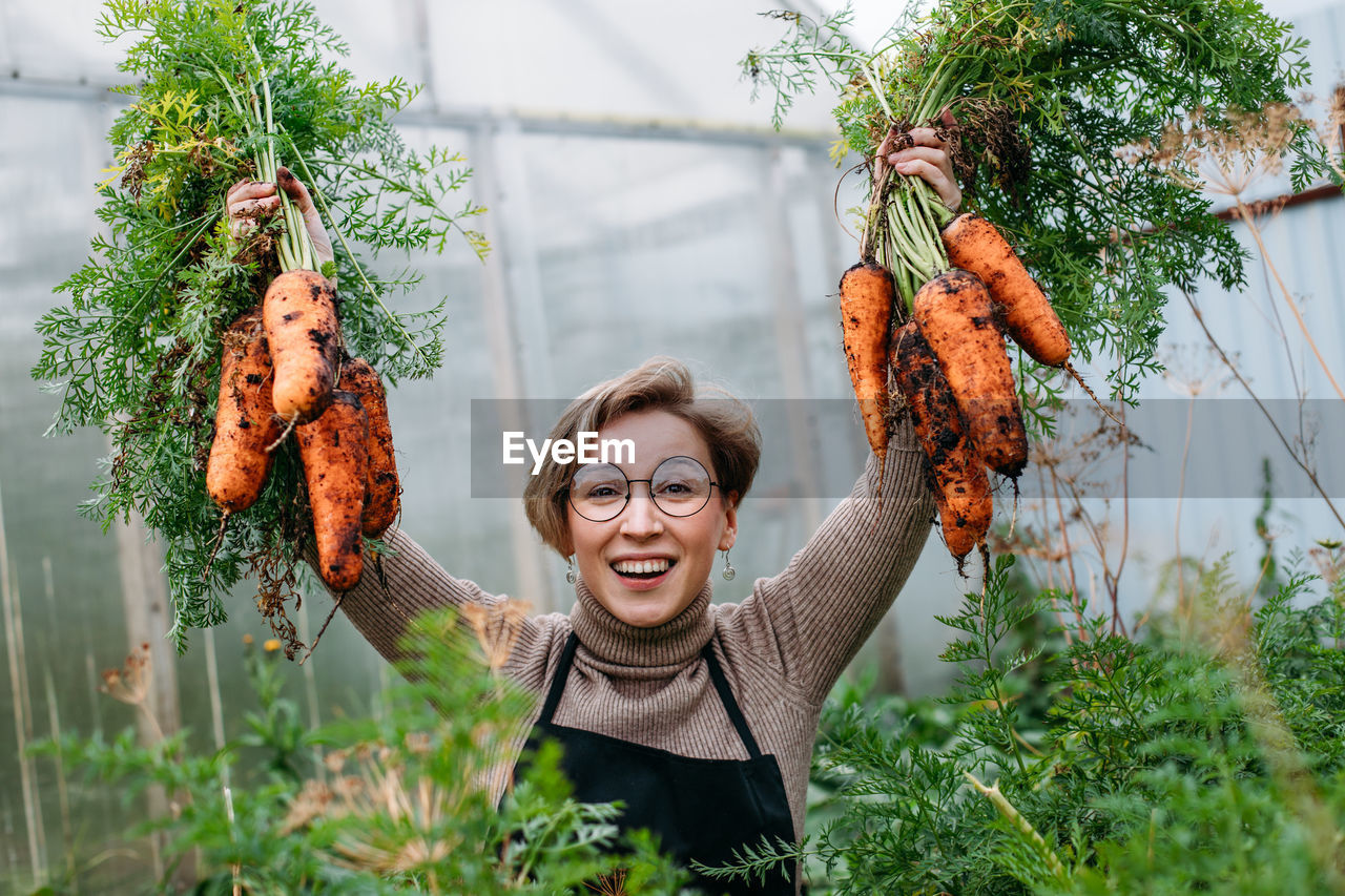 portrait of young woman with arms outstretched standing amidst plants