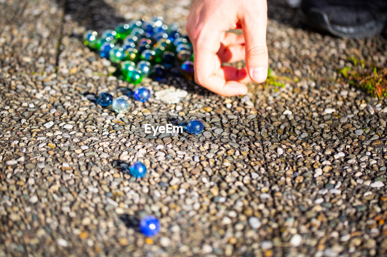 Cropped image of person playing with marbles on footpath