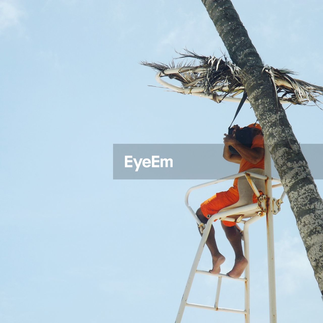 Low angle view of man sitting at lifeguard hut against clear sky