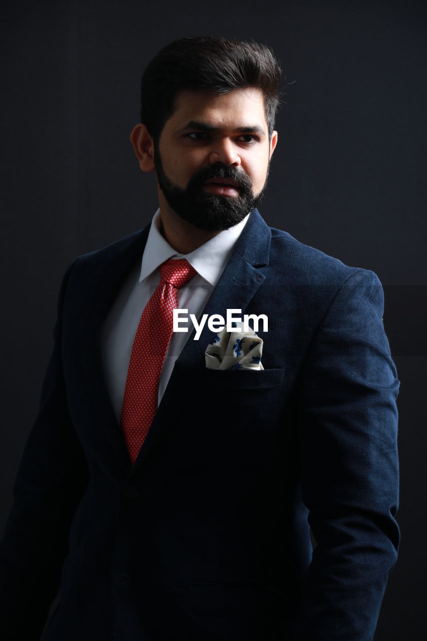 Thoughtful businessman wearing suit while standing against black background