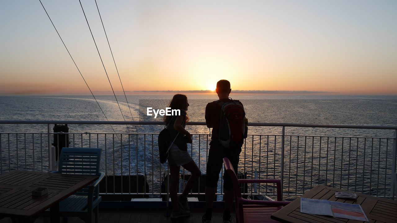 Silhouette people standing by railing against sea during sunset