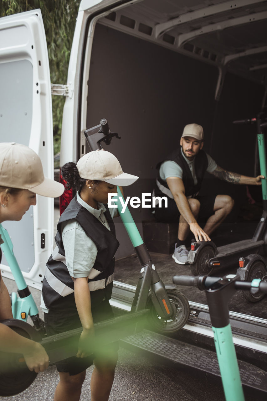 Female delivery workers loading electric push scooters in van