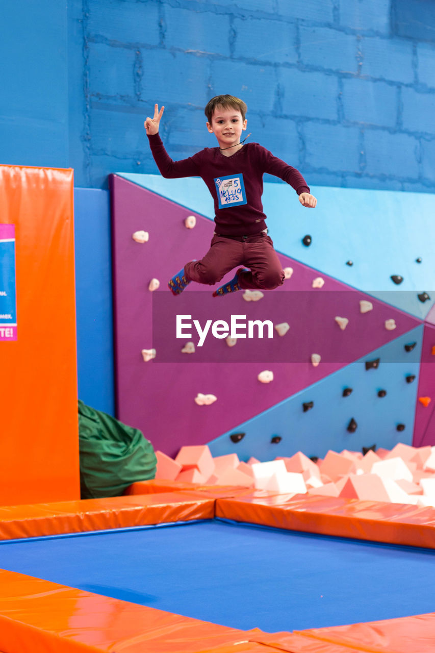 FULL LENGTH PORTRAIT OF BOY PLAYING IN MID-AIR AGAINST WALL