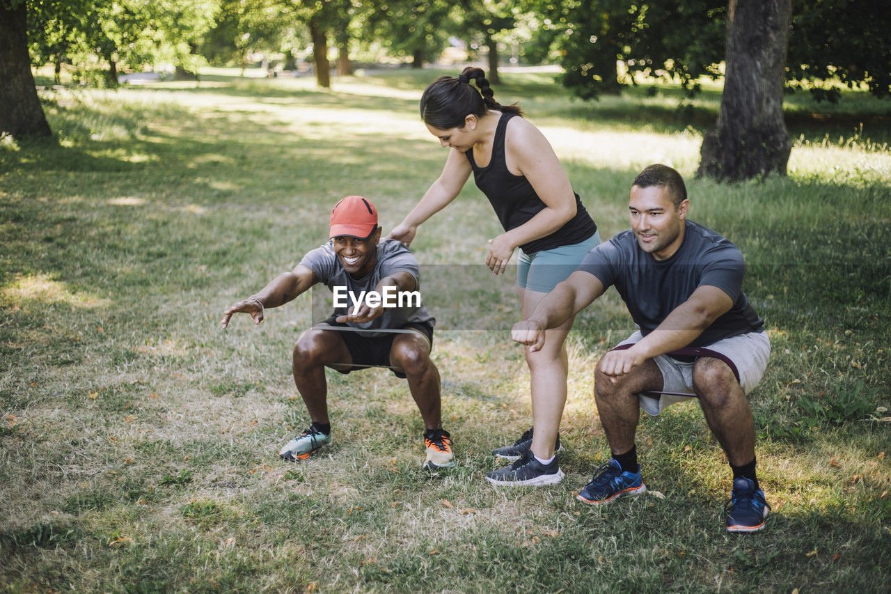 Female coach assisting men practicing squats on grass at park