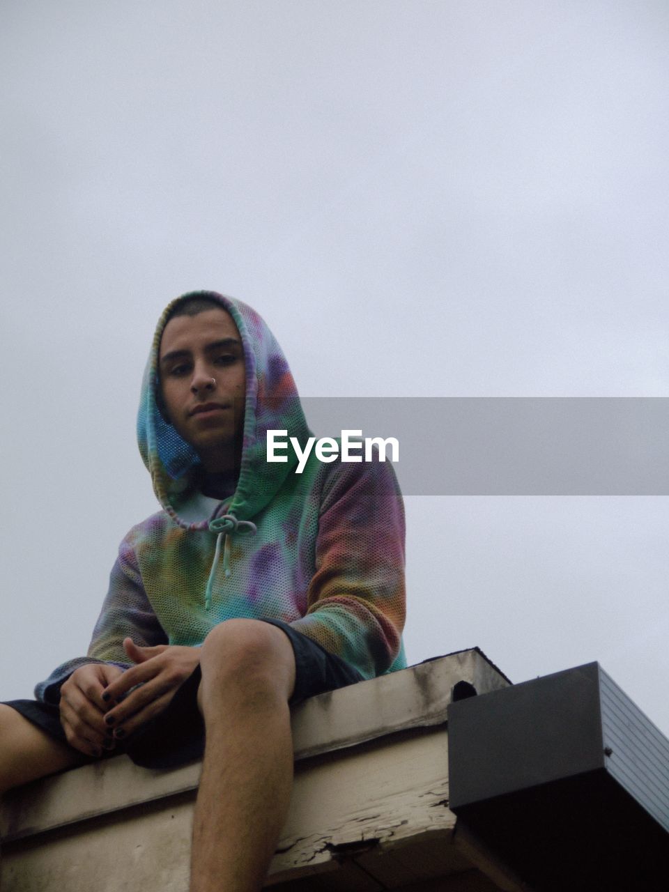 LOW ANGLE VIEW OF MAN SITTING ON LOOKING AWAY AGAINST SKY