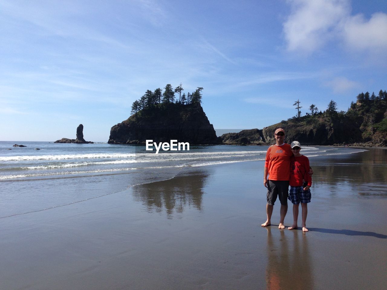 Full length of man and boy standing at beach against sky on sunny day