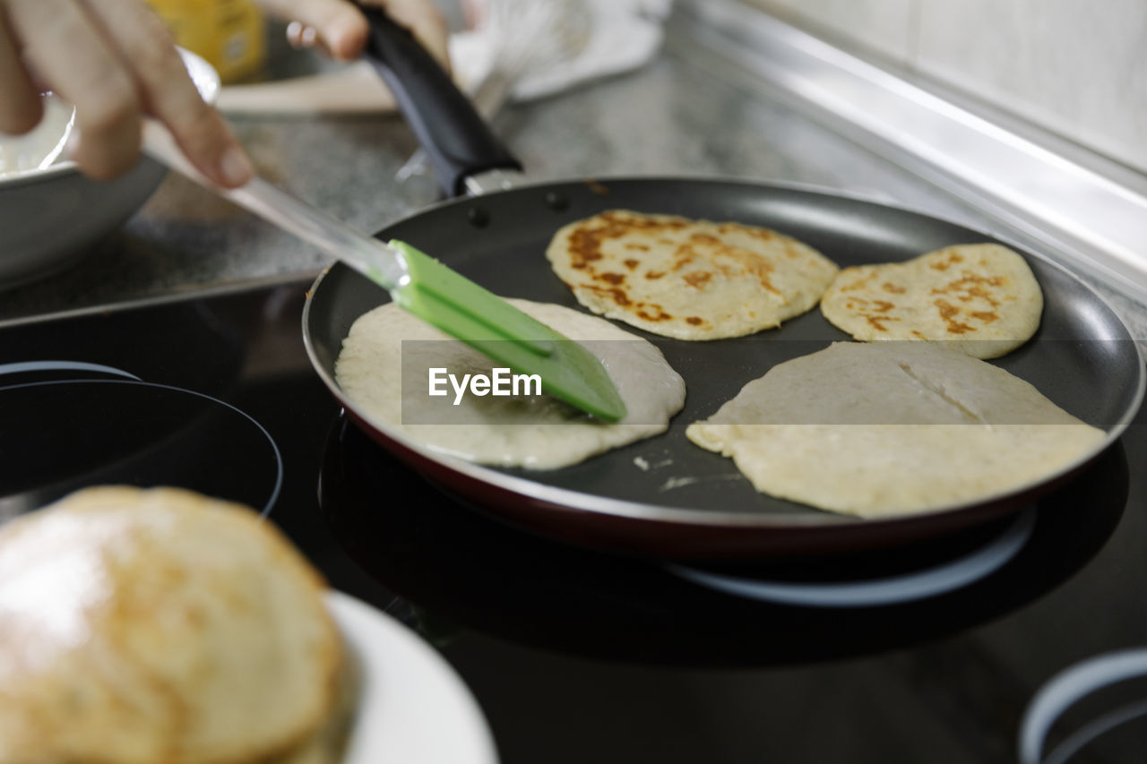 Crop person with spatula frying tasty pancakes on hot pan in kitchen person