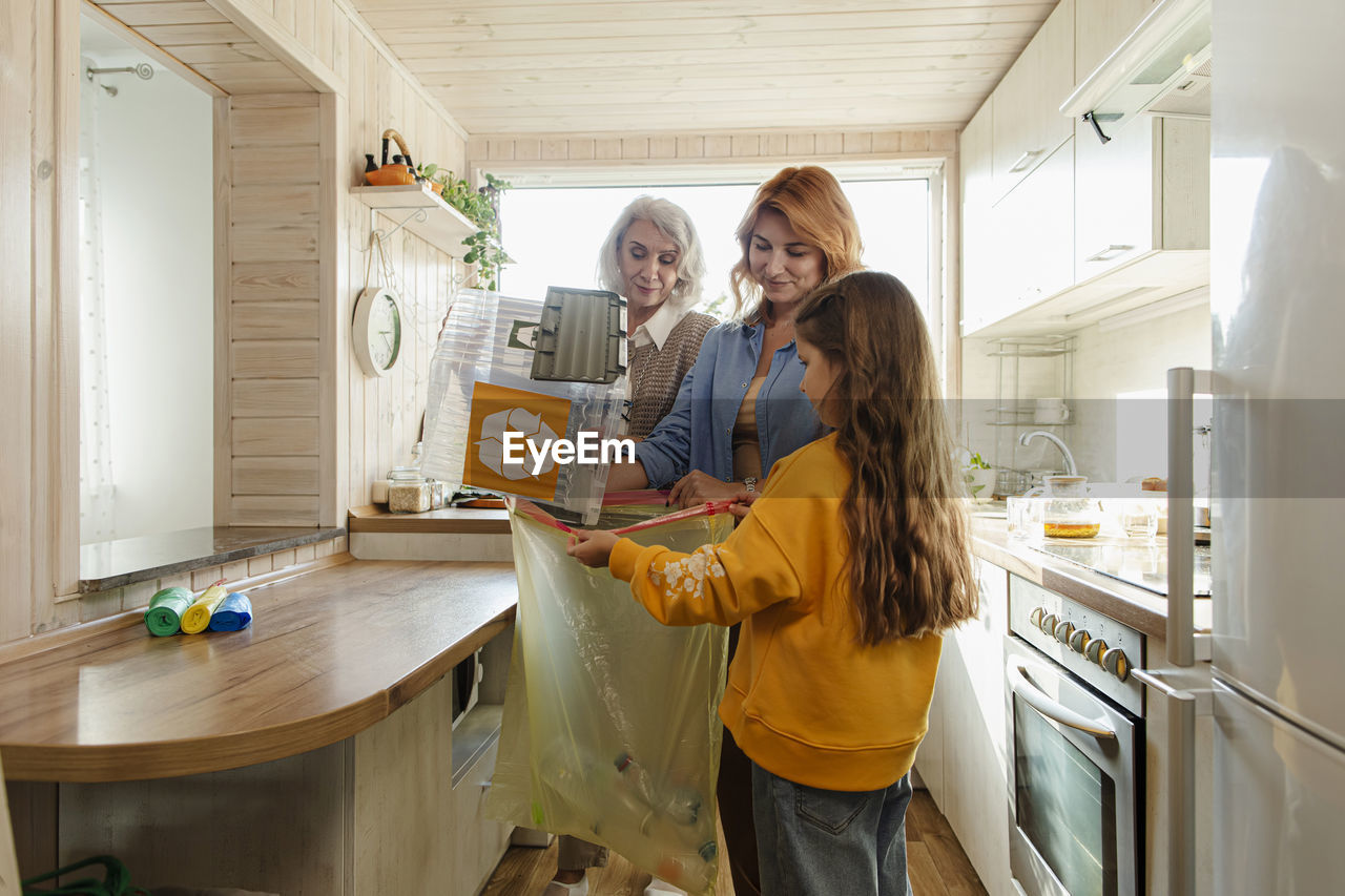 Grandmother, mother and daughter sorting recycling waste in kitchen