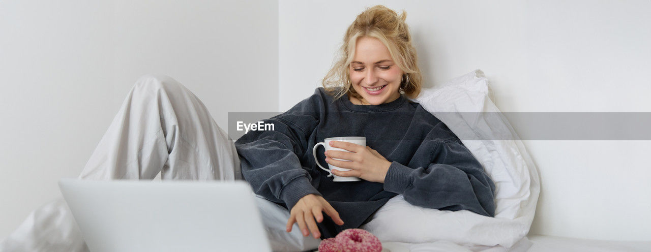 portrait of young woman using digital tablet while lying on bed at home