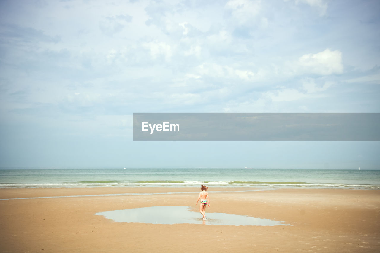 Rear view of shirtless girl walking at beach against sky