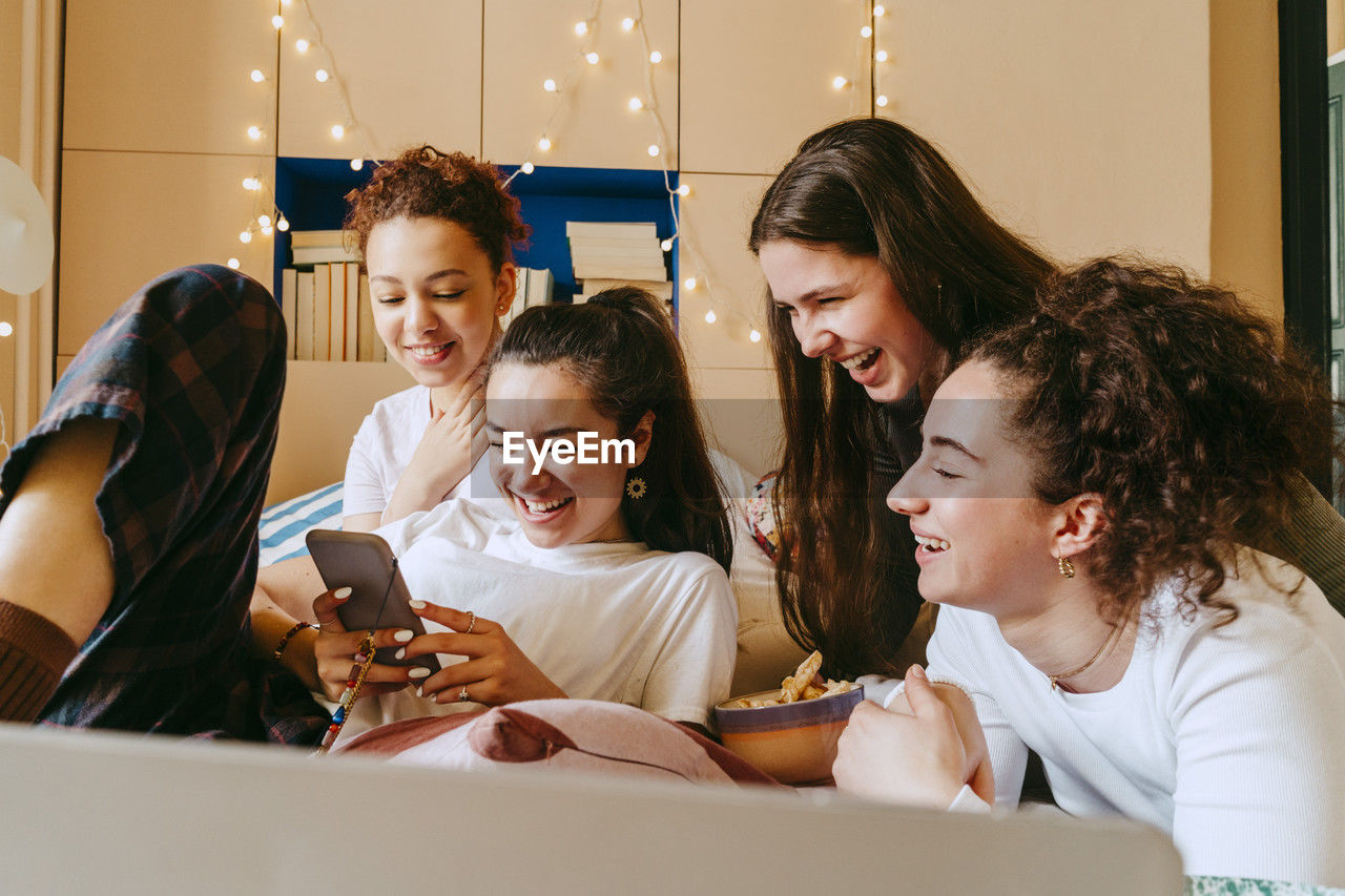 Happy young woman showing smart phone to female friends at home