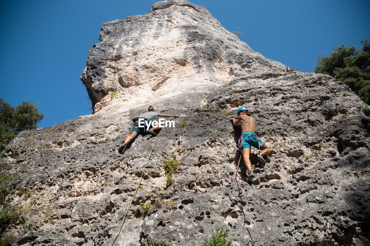 Low angle view of man and woman rock climbing in forest