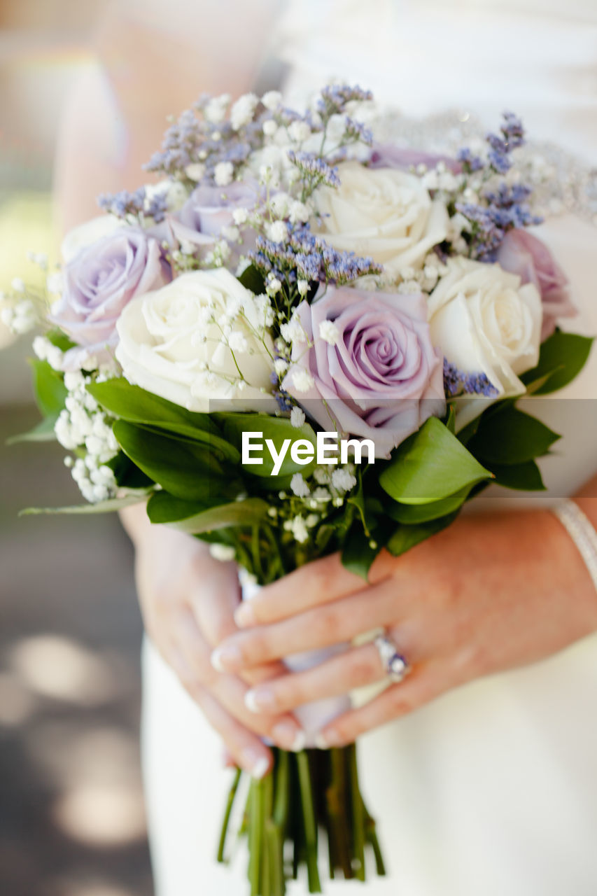 Closeup of bride with wedding bouquet with white, cream, violet roses, out of focus wtih copy space.