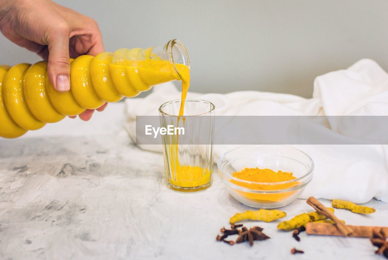 A woman's hand pours a turmeric latte with milk and cinnamon from a bottle into a glass