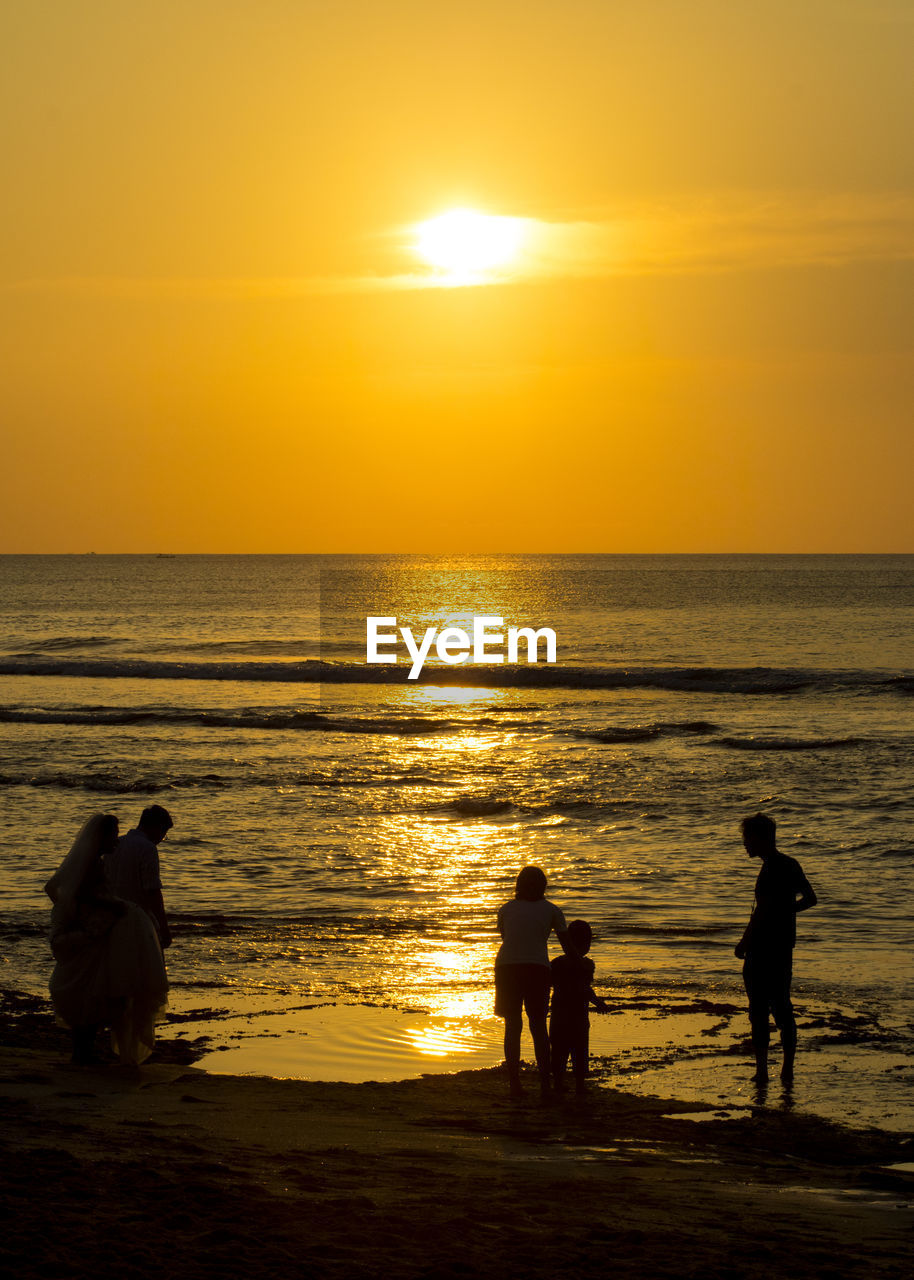 Silhouette people on beach against sky during sunset