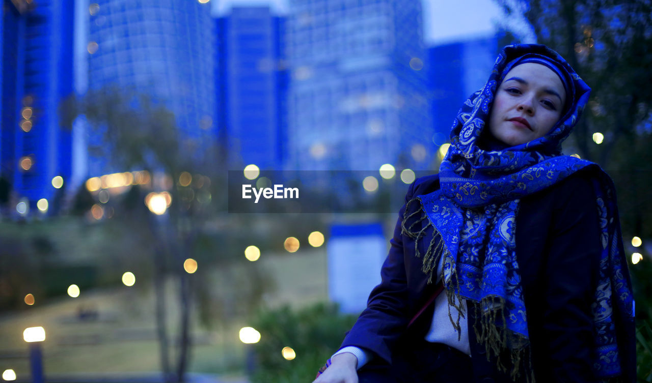 Portrait of young woman looking at illuminated city in winter