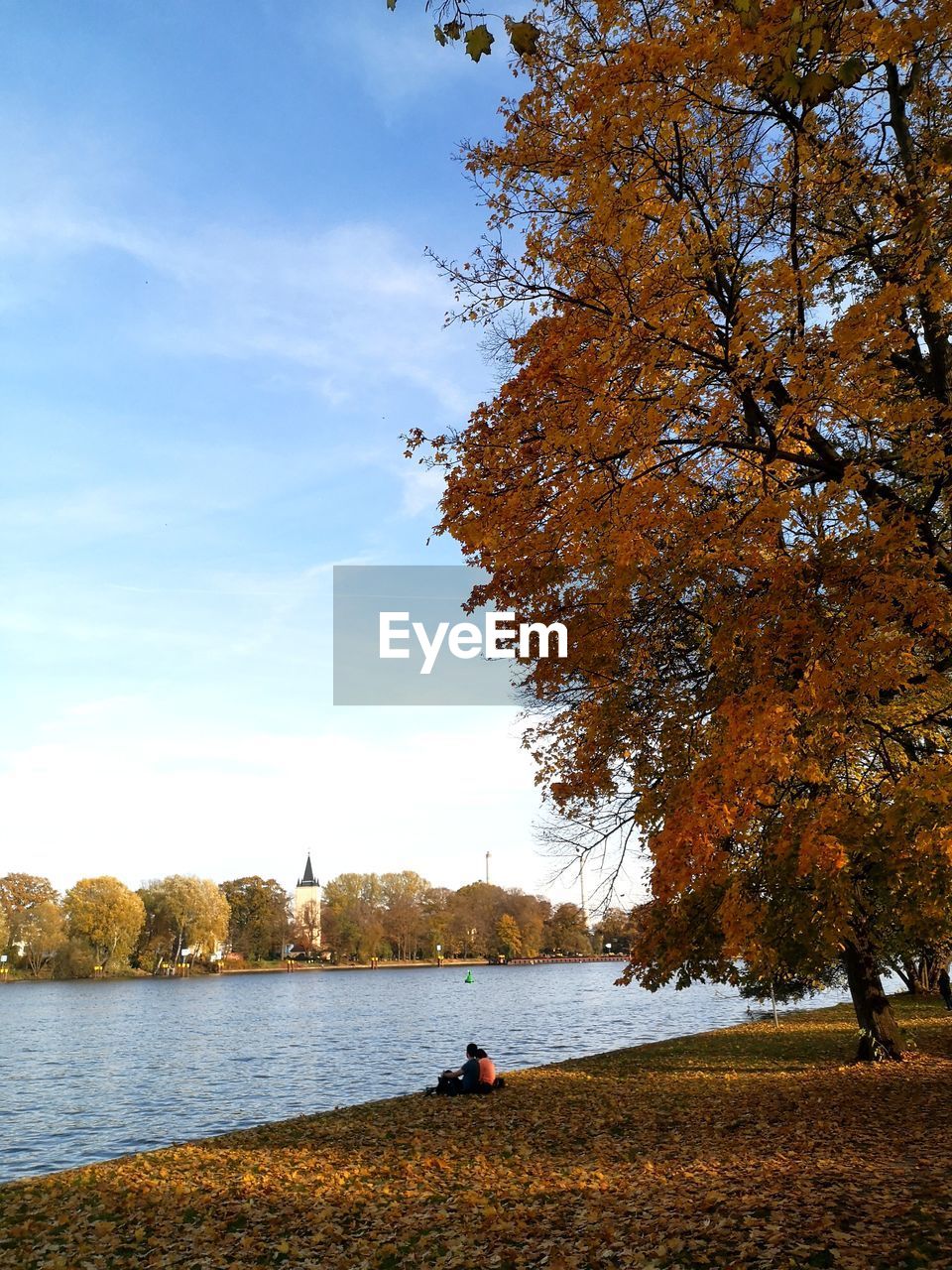 Scenic view of lake in a warm autumn day with a couple sitting near the water