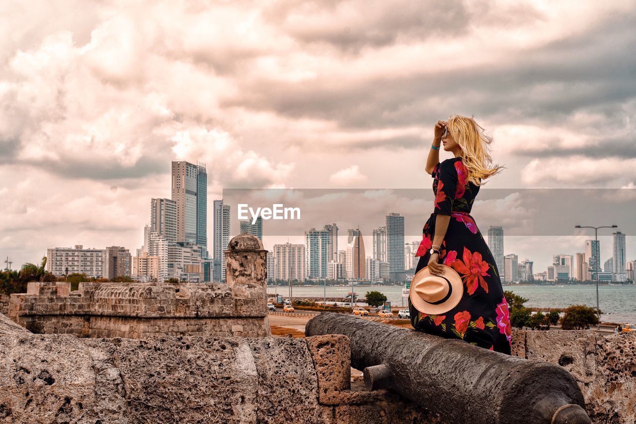 Fashionable woman standing by cannon against sky