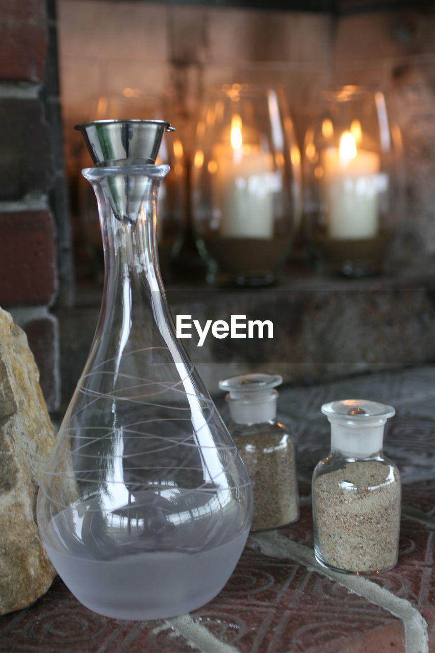 Drink in flask by jars against illuminated candles