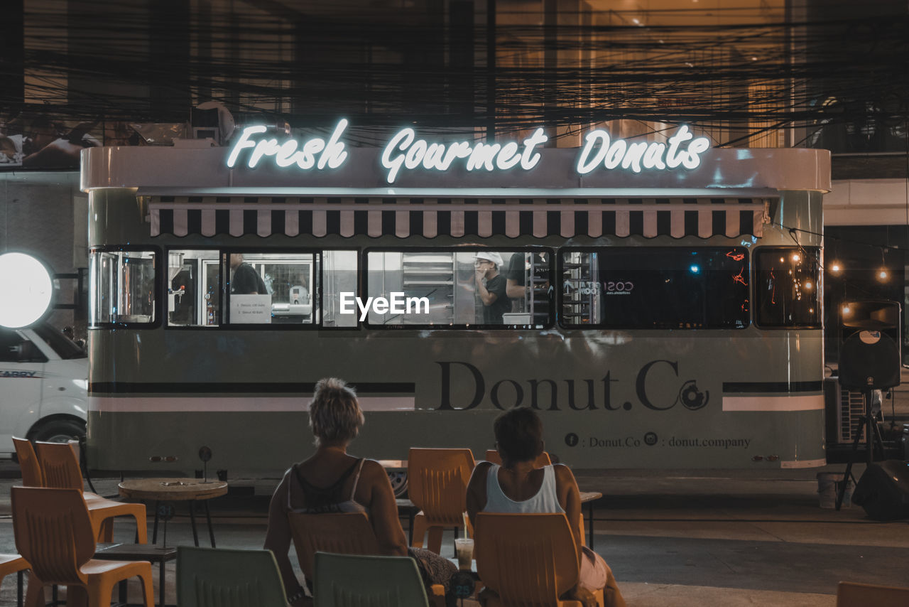 REAR VIEW OF PEOPLE SITTING OUTSIDE RESTAURANT