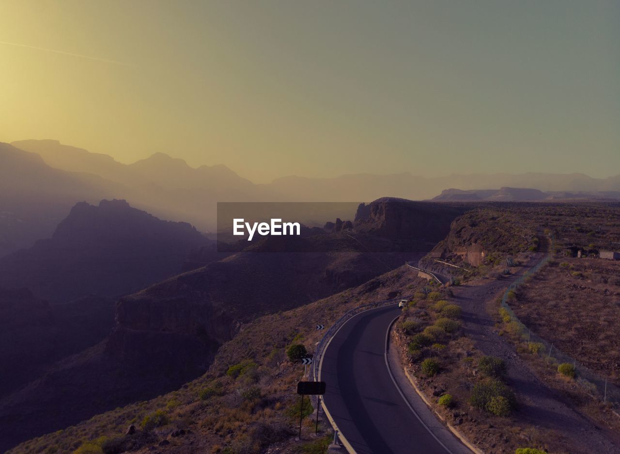 Road leading towards mountains against clear sky