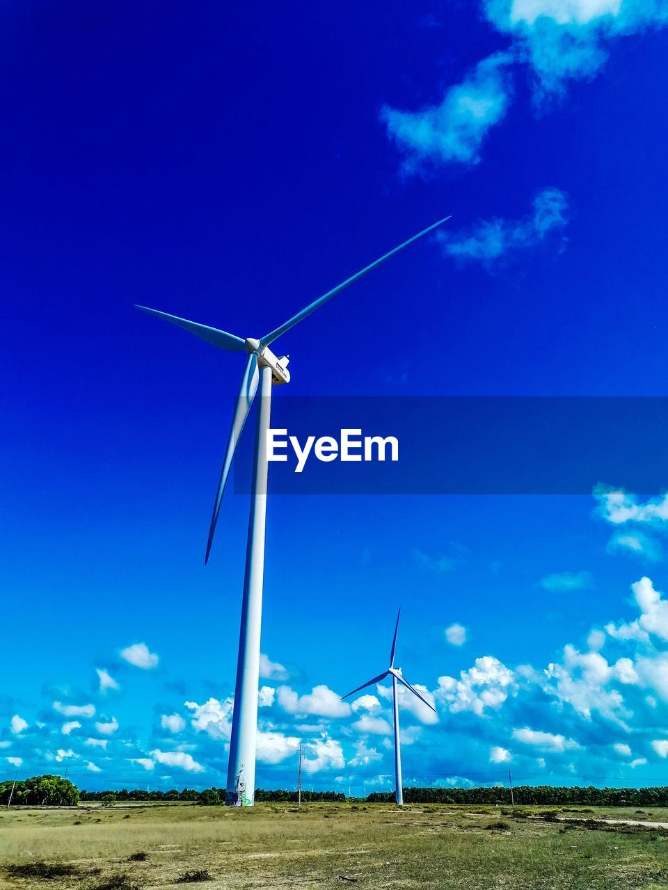 Low angle view of wind turbines on field against blue sky
