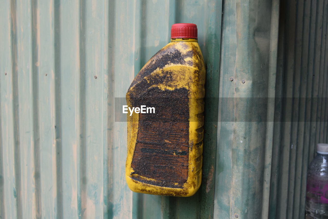 Close-up of old dirty bottle attached on corrugated iron