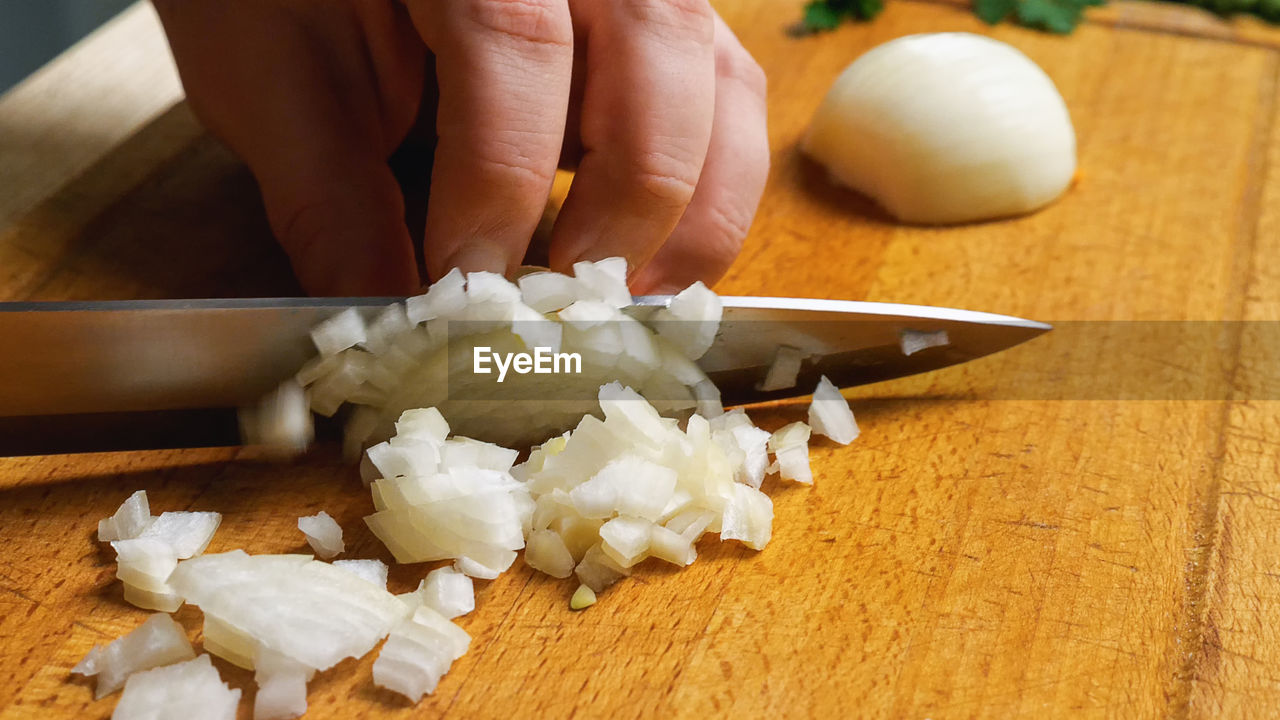 Close-up of a woman's hand with a knife on a cutting board, dicing onions