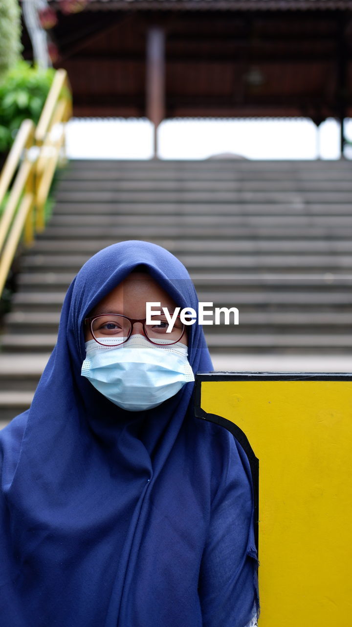 Portrait of a girl wearing blue hijab, sunglasses and disposable mask standing outdoors