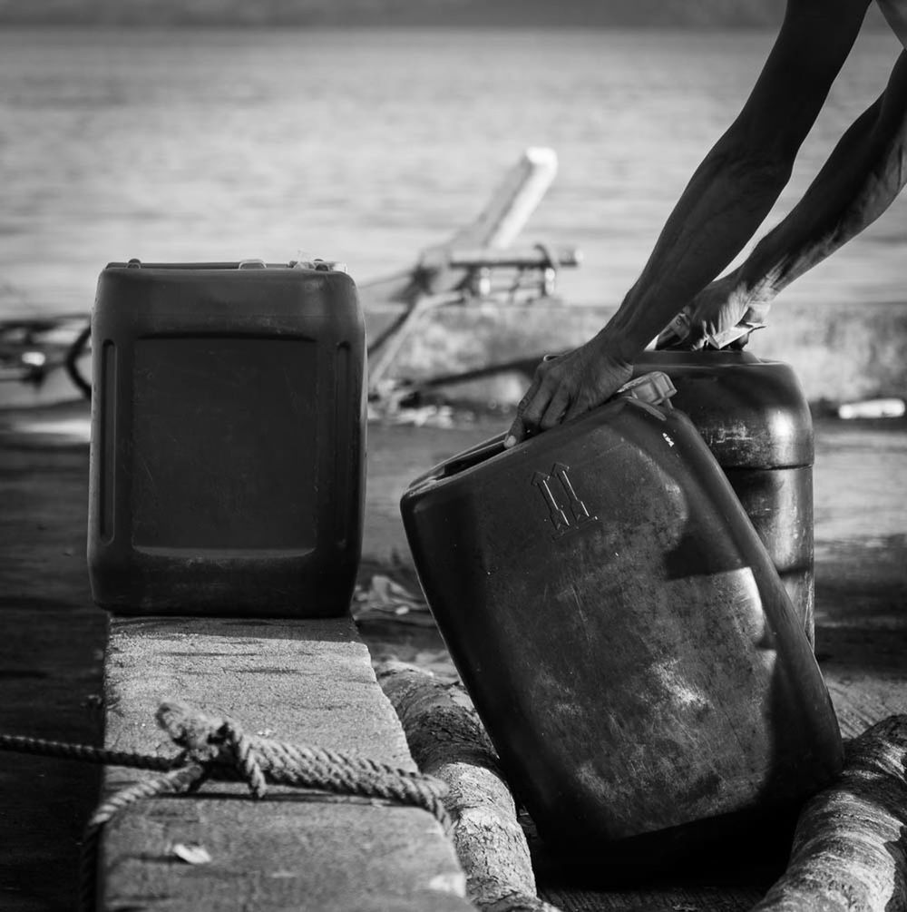 Man loading heavy gallon of fuel can on river bank