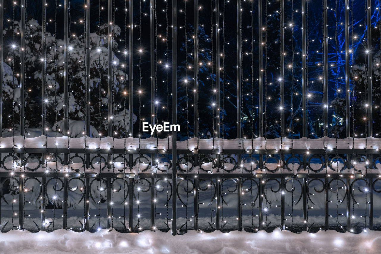 Ornamental, metal fence decorated with led illumination. snow covering metalwork. 