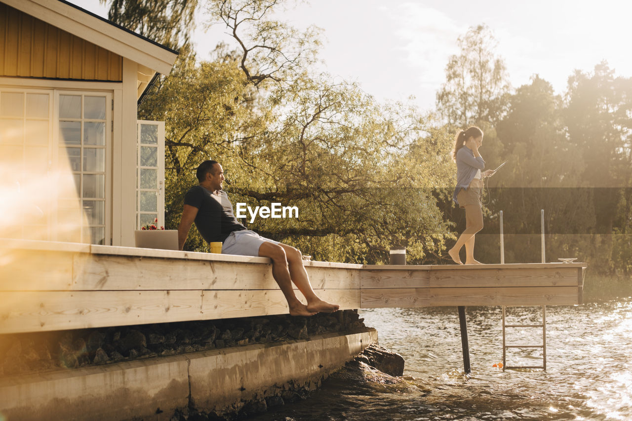 Mature man looking at woman using digital tablet while sitting on patio by lake