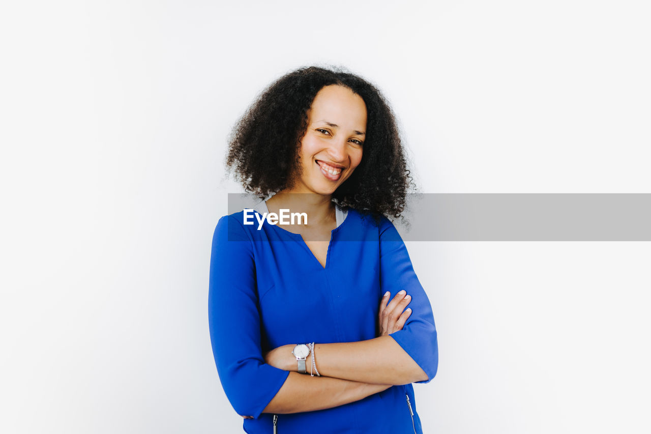 PORTRAIT OF A SMILING YOUNG WOMAN AGAINST WHITE BACKGROUND