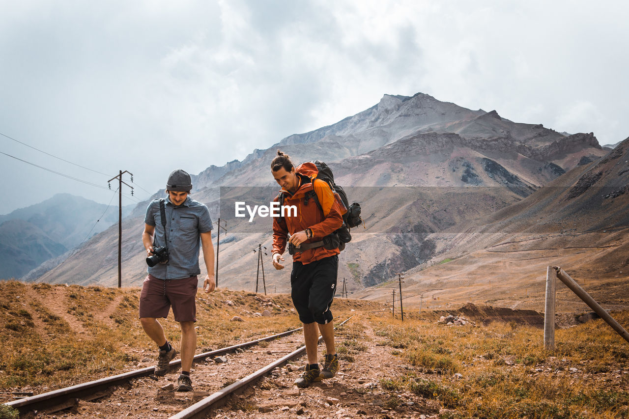 Young friends walking on railroad tracks against mountains