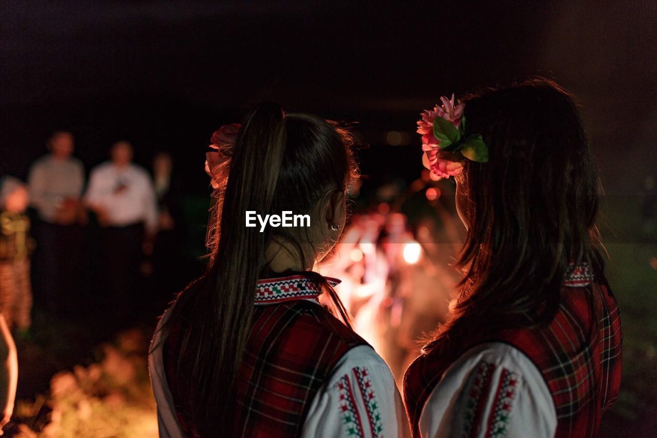Rear view of friends in traditional clothing by campfire at night