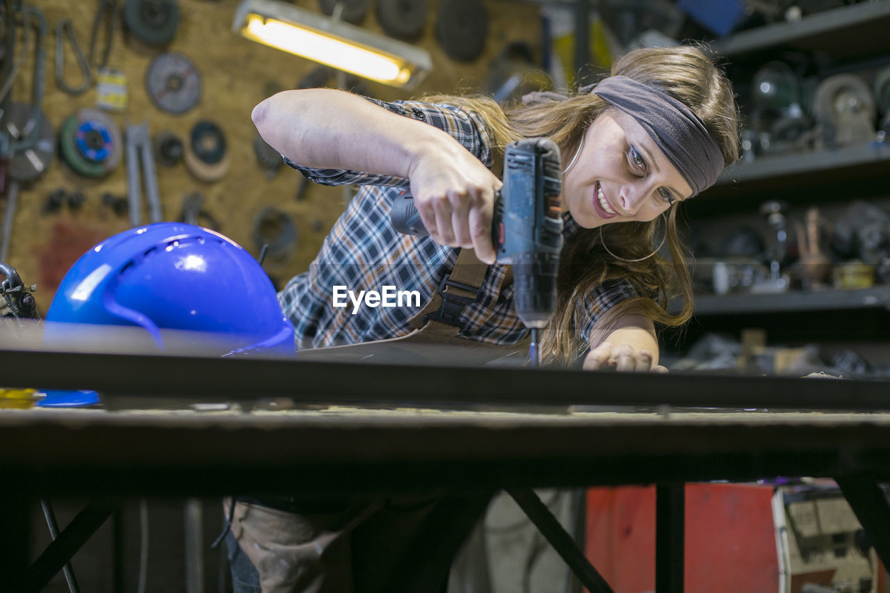 Low angle view of woman drilling on table in workshop