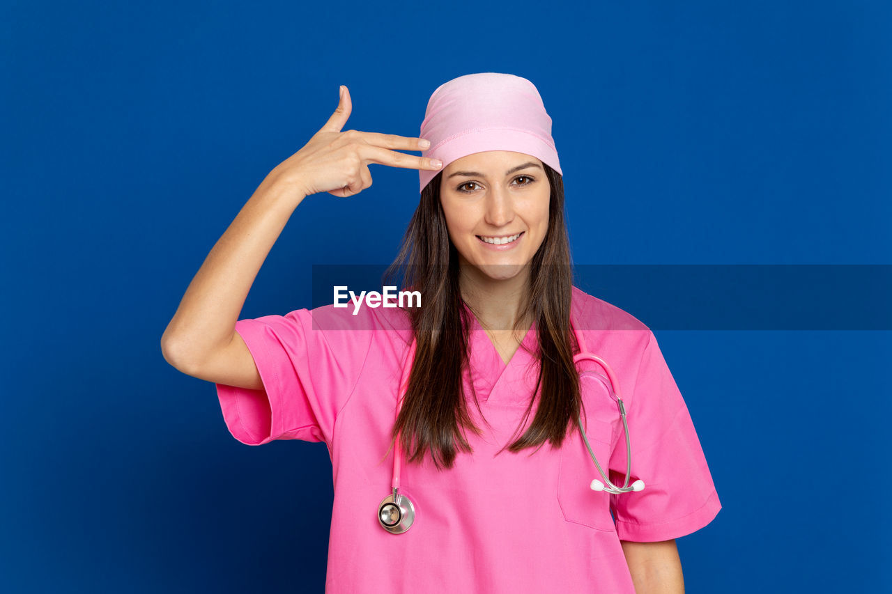 PORTRAIT OF SMILING YOUNG WOMAN STANDING AGAINST PINK BLUE SKY