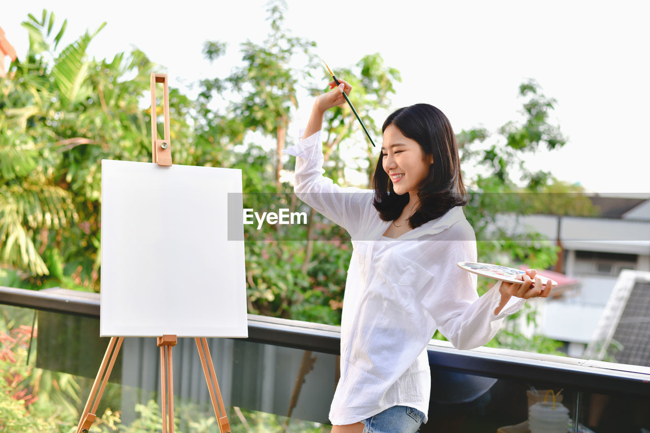 Smiling young woman painting while standing in yard